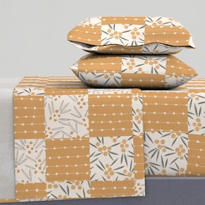 May include: A bed set with a patchwork design in mustard yellow and cream. The pattern incorporates floral and dotted stripe motifs. Two pillows, stacked on top, display the same design. The theme is bedding and home decor, with measurements in centimetres.