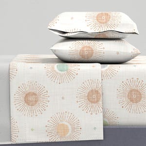 Op de afbeelding: Een wit beddengoedset met een zonnestralenpatroon in tinten oranje en bruin. De set bevat een hoeslaken, een plat laken en twee kussenslopen.