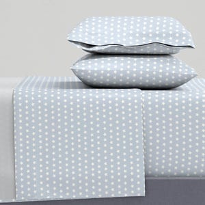 May include: A light blue bed sheet with a white star pattern. The sheet is folded and stacked on top of two matching pillowcases.