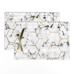 以下が含まれることがあります： 金色の幾何学模様が施された白い大理石のランチョンマット2枚。ランチョンマットは柔らかく耐久性のある生地で作られており、どんなダイニングテーブルにも上品さを添えるのに最適です。