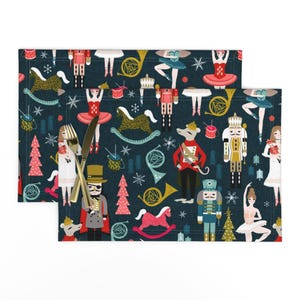 Peut inclure: Un set de table bleu foncé avec un motif répétitif de casse-noisettes, ballerines, chevaux à bascule, instruments de musique et sapins de Noël. Une fourchette et un couteau dorés sont posés sur le côté gauche de la surface en tissu.