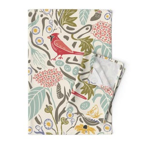Può includere: Un asciugamano da cucina color crema con un motivo floreale e di uccelli colorato. Il motivo presenta cardinali rossi, foglie verdi, fiori rosa e gialli e rami marroni.