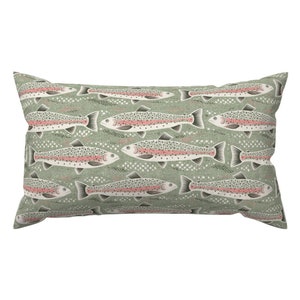 May include: Rectangular pillow with a repeating pattern of rainbow trout on a muted green background. The fish have pink stripes, white spots, and black details. The pillow is a decorative item, suitable for a bed or couch.