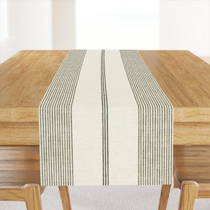 Könnte beinhalten: Ein weißer Tischläufer mit schwarzen Streifen. Der Läufer ist aus einem gewebten Stoff gefertigt und hat eine dezente Textur. Er liegt auf einem Holztisch.