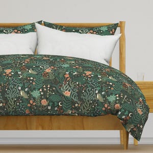 Puede incluir: Una funda nórdica verde y marrón con un patrón floral y criaturas del bosque. La funda nórdica está sobre un marco de cama de madera.