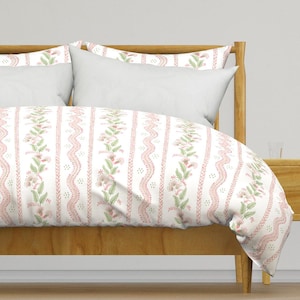 May include: A white duvet cover with a pink and green floral pattern. The duvet cover is on a bed with a wooden headboard and a white pillow.