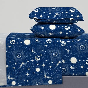 Op de afbeelding: Een blauwe en witte beddengoedset met een hemels patroon met sterren, manen en planeten. De set bevat een plat laken, een hoeslaken en twee kussenslopen.