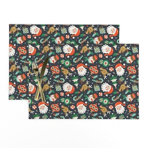 May include: A set of two dark blue placemats with a repeating pattern of Santa Claus, reindeer, candy canes, and ornaments. The pattern is in red, green, white, and gold.