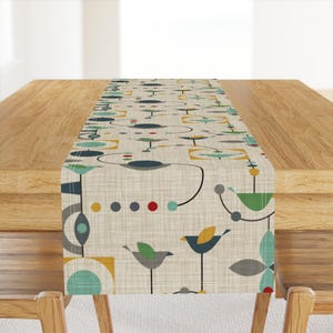 May include: A beige table runner featuring a geometric design of stylised birds, circles and squares in shades of blue, green, yellow, red and grey.