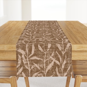 May include: A brown table runner with a white leaf pattern. The runner has a subtle textured look and a stitched border.