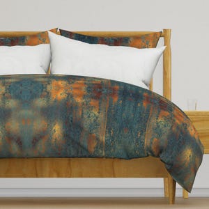 May include: A teal and orange duvet cover with a rusty metal pattern. The duvet cover is on a wooden bed frame with two white pillows.
