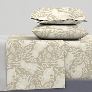 May include: A beige bedding set with a white rabbit and floral pattern. The set includes a fitted sheet, flat sheet, and two pillowcases.