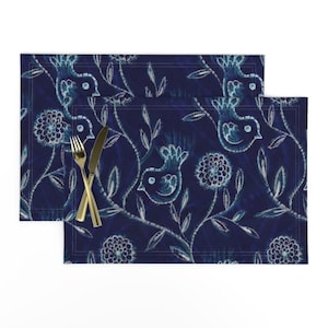 May include: Two blue placemats with a white floral and bird design. The placemats have a dark blue background and a white floral pattern with small birds.