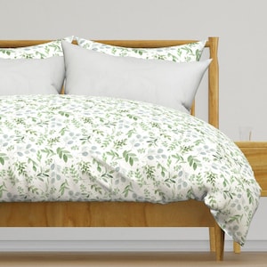 May include: A white duvet cover with a green leafy pattern. The duvet cover is on a bed with a wooden headboard and two white pillows.