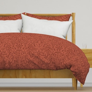 May include: A red patterned duvet cover with a white pillow on a wooden bed frame.