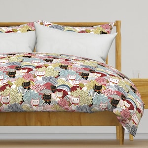Puede incluir: Una funda nórdica blanca con un patrón colorido de gatos y flores. La funda nórdica está sobre un marco de cama de madera con dos almohadas blancas.