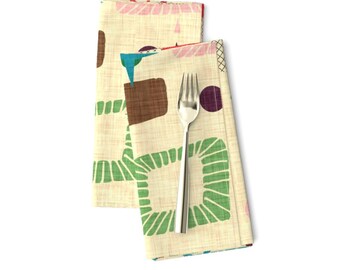 May include: Two beige linen napkins with a geometric pattern of green squares, brown rectangles, and colorful circles. The napkins are folded and a silver fork is placed on top.