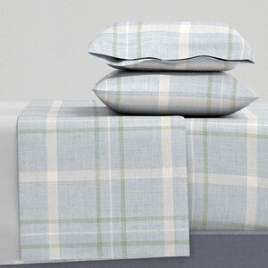 May include: Two rectangular bed pillows stacked on top of a flat bed sheet. The bedding set features a light blue, white, and sage green plaid pattern with a woven texture. The pillows are plump and rectangular, resting on the smooth, draped sheet.