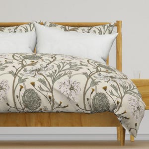 May include: A bed with a wooden frame and a floral patterned duvet cover. The cover features a cream background with a repeating pattern of white flowers, green leaves, and brown stems. White pillows are on the bed.