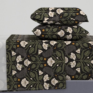 May include: A bedding set featuring two stacked pillows and a flat sheet with a black background. The pattern consists of white flowers, green leaves, small yellow circles, and dark grey birds arranged in a repeating botanical design.
