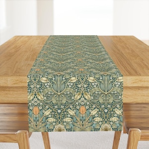 May include: A rectangular table runner featuring a repeating botanical pattern of cream-colored tulips, sage green leaves, and small white flowers set against a dark teal background, finished with a thin white border along the edges.