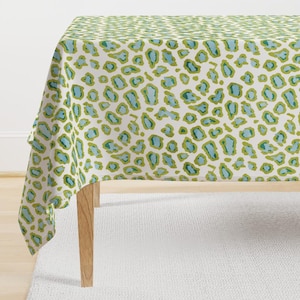 May include: A white tablecloth with a green and blue leopard print pattern. The tablecloth is draped over a table with wooden legs.