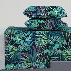 Puede incluir: Una sábana de cama azul oscuro y dos fundas de almohada con un patrón de hojas tropicales en tonos de verde, turquesa y morado.