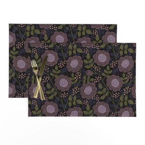 May include: Two dark purple floral placemats with a repeating pattern of stylized flowers and leaves. The placemats have a dark background and are made of a fabric material.