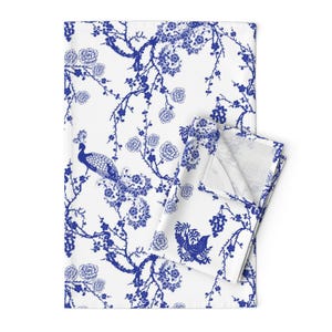 May include: Blue and white kitchen towel with a floral and peacock design. The towel features a repeating pattern of stylized flowers and branches with a peacock perched on a branch.