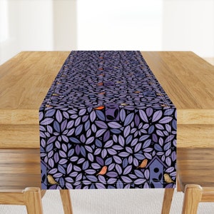 May include: Purple table runner with a pattern of leaves and birds. The leaves are a dark purple color and the birds are a light brown color. There are also small white dots scattered throughout the pattern.