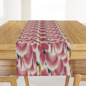May include: A pink and white table runner with a repeating pattern of abstract shapes. The runner has a subtle sheen and a slightly textured surface.