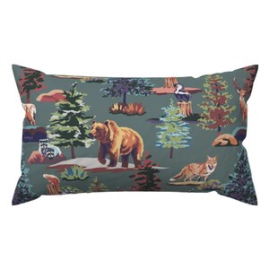 May include: Rectangular pillow with a forest scene print. The design features a brown bear, a coyote, a raccoon, and a deer among trees and foliage. The background is a muted teal color.
