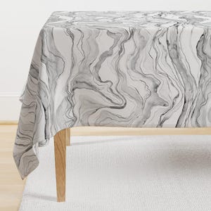 May include: A white tablecloth with a black and gray marbled pattern. The tablecloth is draped over a wooden table.