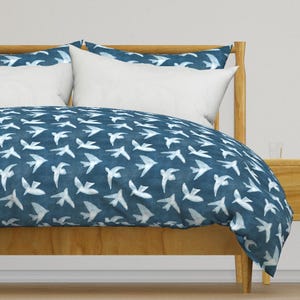 May include: A blue duvet cover with a white bird pattern. The duvet cover is on a wooden bed frame with white pillows.