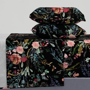 Puede incluir: Un juego de cama floral negro con un fondo oscuro y una variedad de flores rosas, rojas y verdes. El juego incluye una sábana plana, una sábana bajera y dos fundas de almohada.