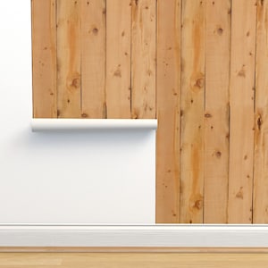May include: A close-up of a wood plank wallpaper with a light brown color. The wallpaper is partially unrolled, revealing a white wall behind it.