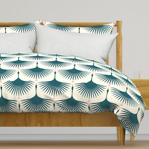 Op de afbeelding: Een witte dekbedovertrek met een teal en rood kraanvogelpatroon. De dekbedovertrek ligt op een bed met een houten hoofdbord en een wit kussen.