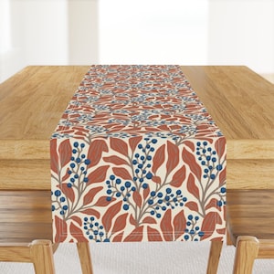 May include: A beige table runner with a repeating pattern of red leaves and blue berries. The runner is 14 inches wide and 70 inches long.