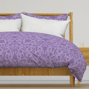 May include: A purple duvet cover with a floral pattern on a wooden bed frame.