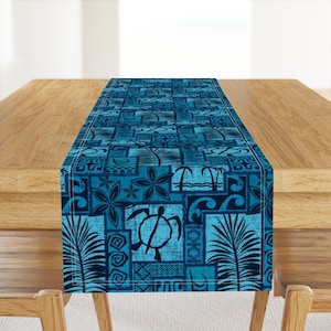 May include: A blue table runner with a Hawaiian-inspired design featuring palm trees, waves, and a turtle. The design is in a patchwork style with various geometric shapes.