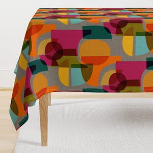 May include: A tablecloth with a geometric pattern featuring overlapping circles and squares in shades of orange, yellow, red, green, and blue on a grey background.