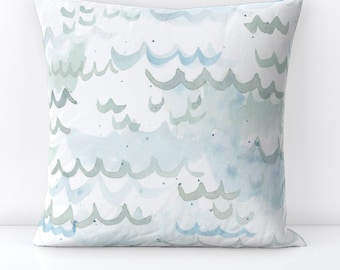 Puede incluir: Una almohada blanca con un diseño de acuarela de olas azules y verdes.