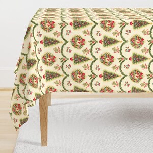 May include: A cream-colored tablecloth with a repeating pattern of Christmas trees, wreaths, and ornaments. The design includes red bows, green garlands, and colorful baubles. The tablecloth is draped over a wooden table.