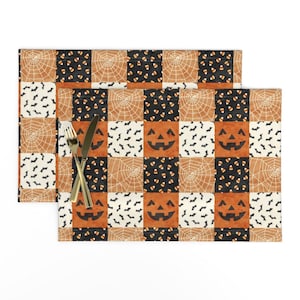 Puede incluir: Un mantel individual rectangular con un patrón de cuadrícula de cuadrados alternos con motivos de Halloween, incluyendo caras de calabaza naranjas, telarañas blancas sobre naranja, murciélagos negros sobre blanco y dulces sobre negro.