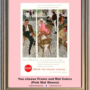 May include: Framed vintage Coca-Cola advertisement featuring a Parisian cafe scene with people enjoying drinks. The ad includes the Coca-Cola logo and text "Sign of Good Taste." The frame is a light brown color, and the mat is pink.