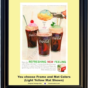 May include: Framed vintage Coca-Cola advert showing three ice cream floats with cherries and mint. The ad text includes "Refreshing New Feeling" and "Tan' ta li zing!" The frame is black, and the mat is light yellow.
