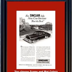 May include: Framed vintage Sinclair Oil advertisement. The black and white ad features a classic car, a devilish figure, and text that reads "How Sinclair helps New Car Owners Beat the Devil." The frame is black, and the mat is maroon.