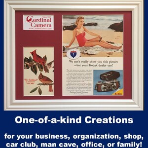 May include: A white framed display featuring a Cardinal Camera logo, a vintage print of two red cardinals, and a Kodak advertisement showing a person in a red swimsuit on a beach with a stereo camera and the text We can't really show you this picture.