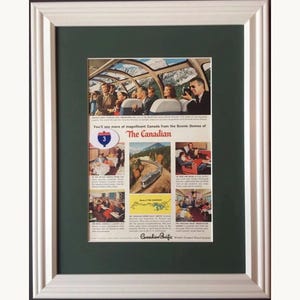 May include: A vintage Canadian Pacific advertisement for The Canadian train service, framed in a white wooden frame with a dark green mat. The print features multiple scenes of passengers in scenic dome cars, dining, and a map of the train route.
