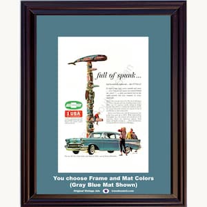 May include: A framed vintage advertisement for a Chevrolet car featuring a tall, colorful totem pole illustration, a light blue sedan, and people standing nearby. The text reads full of spunk and includes the Chevrolet logo and 1 USA of Chevrolet.